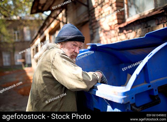 Homeless old man in search for food. Poor tramp hungry, rummaging for some food in garbage
