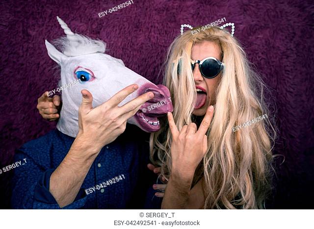 Two funny persons on the purple background shows emotions. Crazy unicorn with expressive young woman in sunglasses and kitty ears