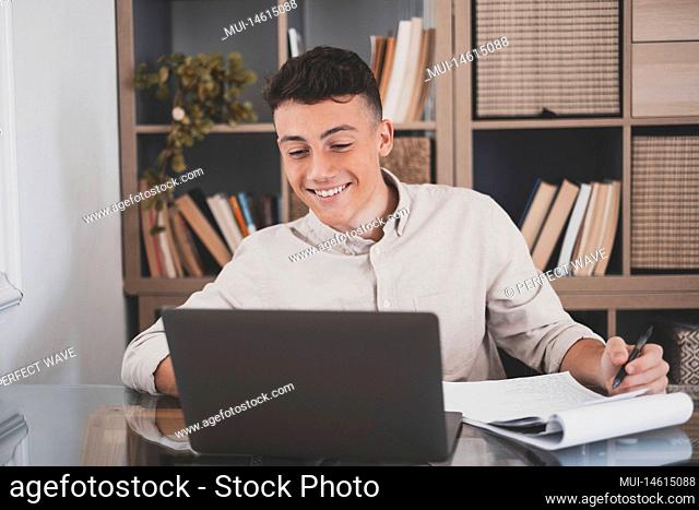 Happy young caucasian businessman smiling working online watching webinar podcast on laptop and learning education course conference calling make notes sit at...