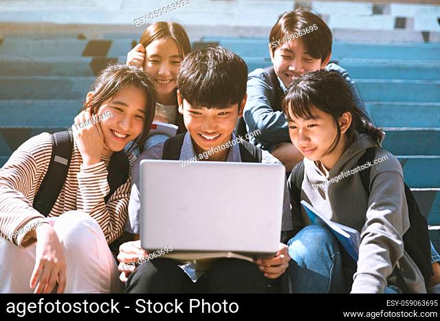 Happy young students looking at laptop and sitting on the stairs
