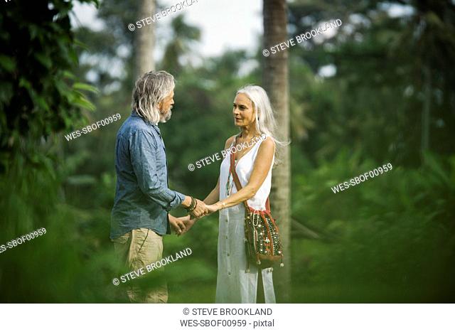 Affectionate senior couple holding hands in tropical landscape with palm trees