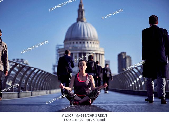 A woman meditating on the Millennium Bridge with St Paul's Cathedral in the background