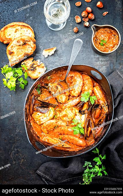 Traditional Catalan fish stew romesco de peix with prawns, mussels and fish as top view in a modern design cast-iron roasting dish