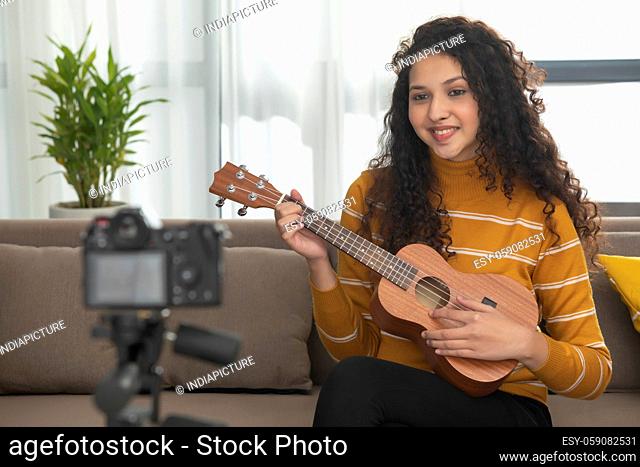A HAPPY TEENAGE GIRL PLAYING UKELELE IN FRONT OF CAMERA AND RECORDING IT