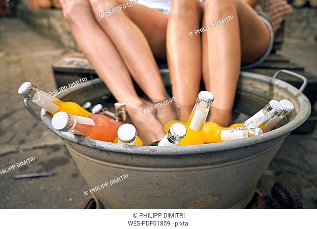 Friends relaxing in a backyard in summer, young women cooling their feet in a tub with drinks