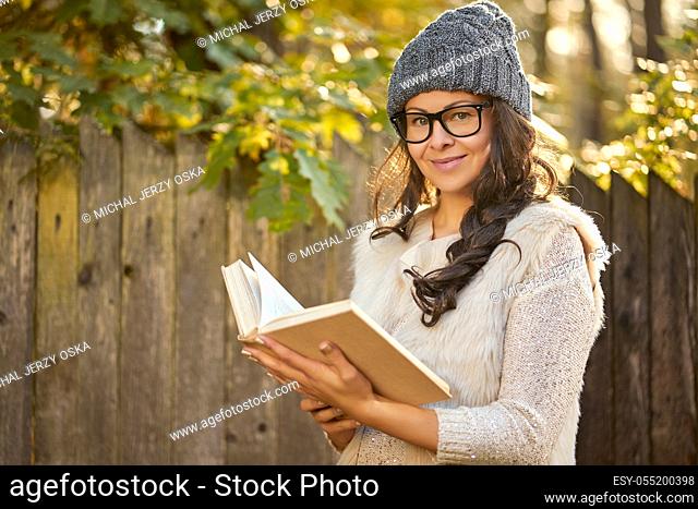 beautiful woman in a cap and glasses is holding a book in an autumn forest in hands