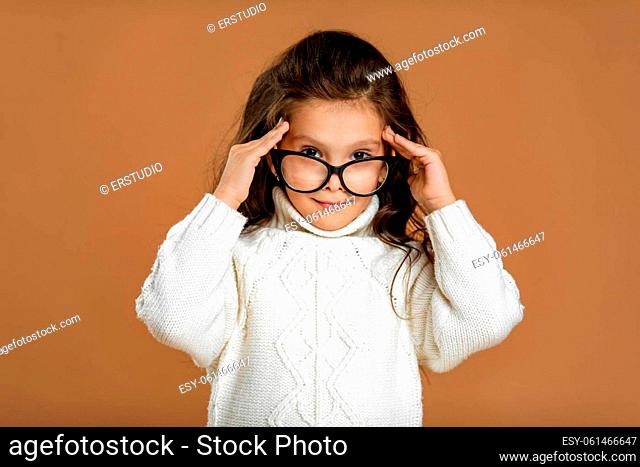 Cute curly little child girl wearing glasses and looking to camera in studio