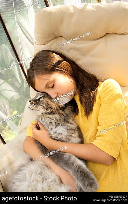 Girl with eyes closed embracing cat on hanging chair
