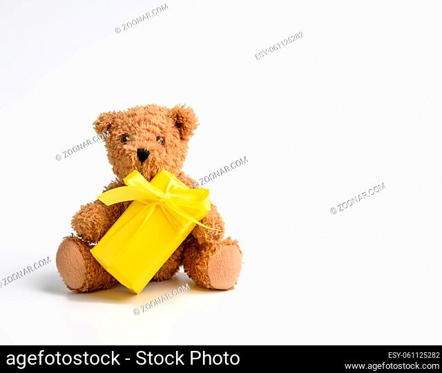 little teddy bear sits on a white background with a gift wrapped in yellow paper and yellow ribbon, copy space