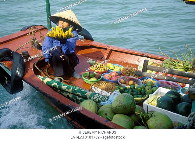 Woman in long flat bottomed boat. Floating fruit stall. Coconuts, bananas