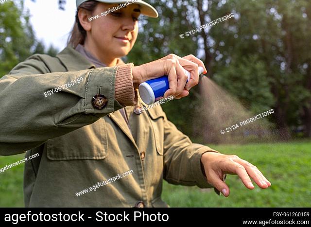 woman spraying insect repellent to hand at park