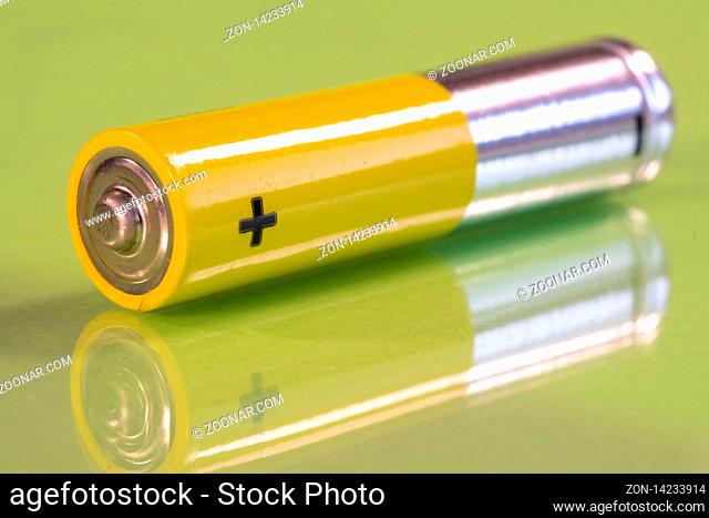 Single AAA battery is seen on a reflective green surface. Closeup view from the plus side of the battery
