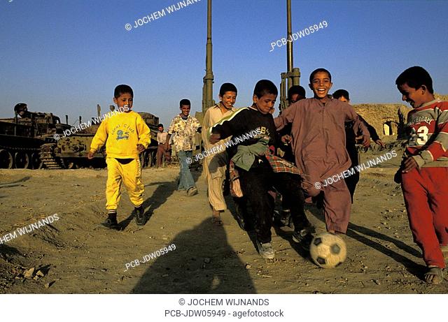 Kabul, children playing soccer between destroyed weaponary