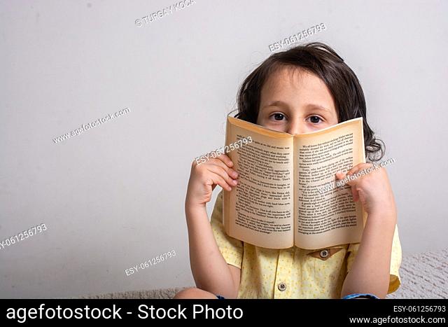 Boy covering face with book as education studying concept