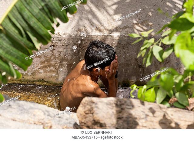 Arabia, Arabian peninsula, Sultanate of Oman, Nizwa, Misfat Al Abreyeen, boy refreshes himself in artificial watercourse