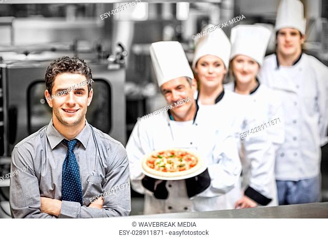 Manager standing in front of chefs holding pizza in kitchen