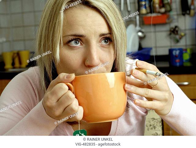 GERMANY : Young woman with a cigarette drinking a cup of tea in her kitchen . - Koeln, GERMANY, 24/07/2007