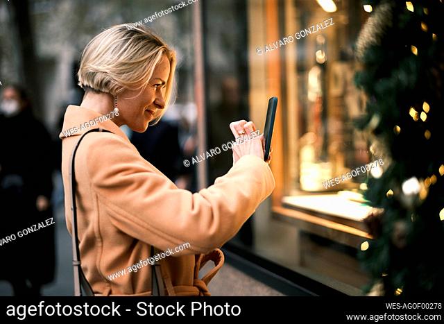 Smiling woman taking picture of Christmas tree through mobile phone