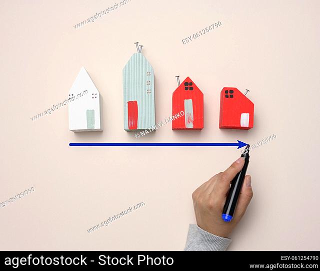 A miniature wooden house and a woman's hand draws a graph with growing indicators. The concept of increasing the value of real estate and rent