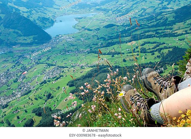 Hiking boots and flowers over the valley on Grosser Mythen peak nearby Schwyz in Alps in Switzerland
