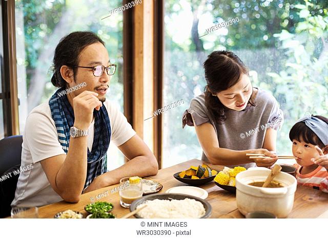 Man, woman and young girl sitting round a table with bowls of food, eating together