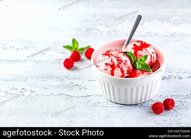 Raspberry ice cream balls with syrup, berries and mint leaves in white bowl