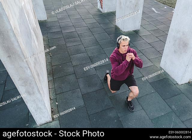 Young athletic man with headphones listen to music and warming up outdoors. Do lunge