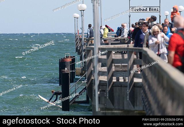 31 May 2020, Mecklenburg-Western Pomerania, Binz: Tourists walk over the pier while a surfer lets his board into the water