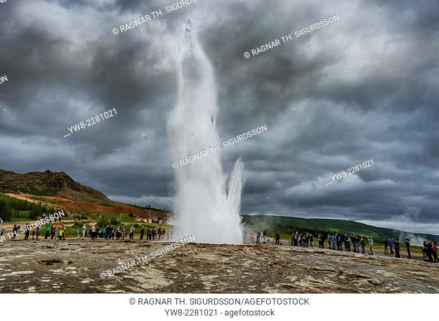 Tourist watching Strokkur Geyser erupting, Iceland. Strokkur is a fountain geyser in the geothermal area beside the Hvita River in the Haukadalur valley