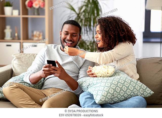 african couple with popcorn and smartphone at home