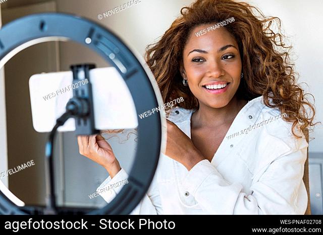 Smiling woman live streaming through mobile phone at home