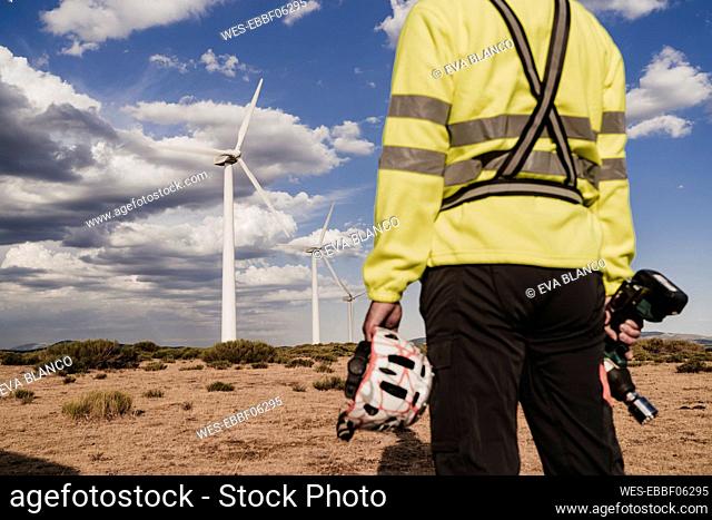Technician holding work tool and helmet standing at wind farm