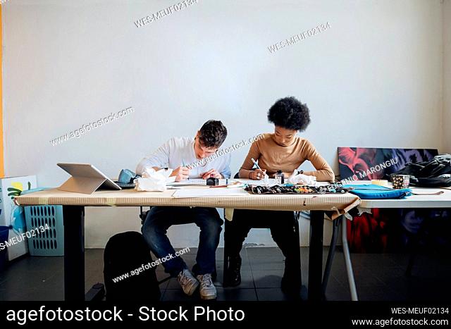 Young multi ethnic couple practicing calligraphy together sitting at table in studio