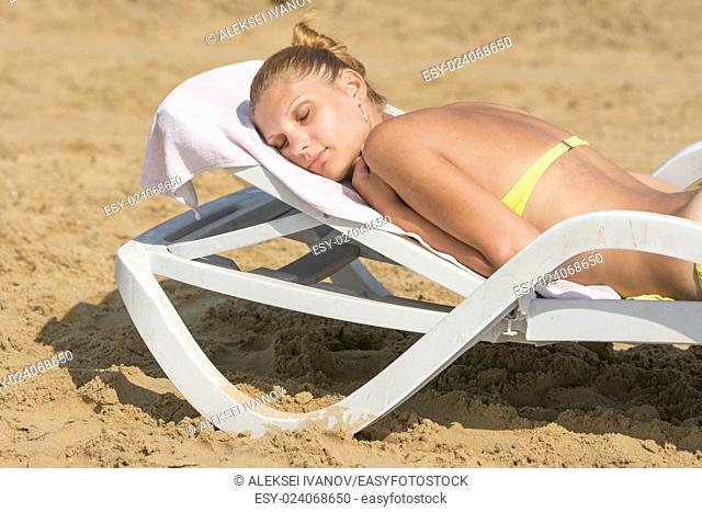Young tanned woman lying on a deck chair with his eyes closed on the beach
