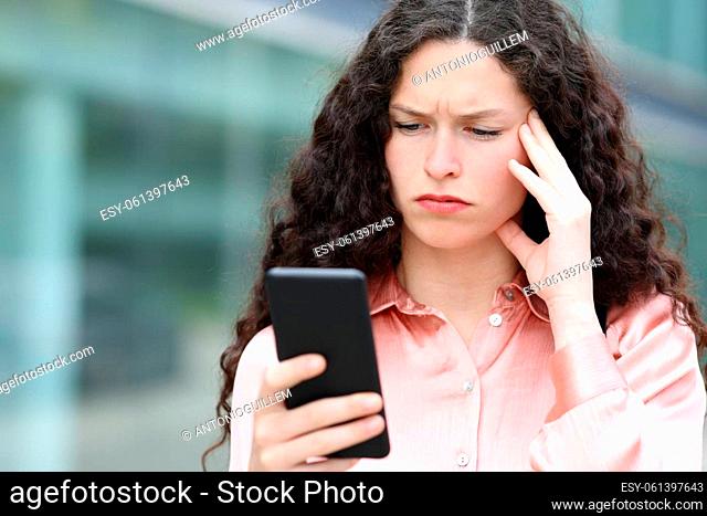 Worried woman reading message on smart phone walking in the street