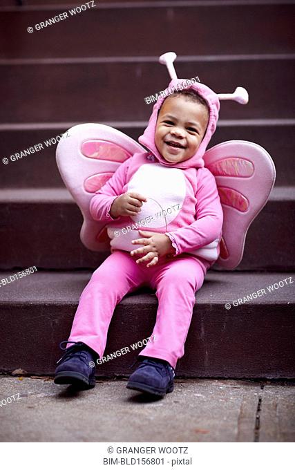 Mixed race girl wearing pink butterfly Halloween costume on staircase