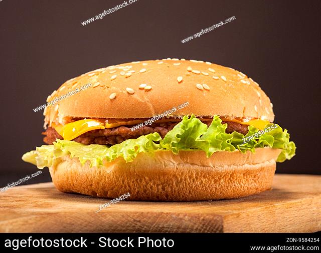 Fresh delicious burger with cheese, onion and lettuce on brown background with copy space