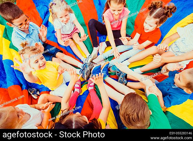 Kids holding hands together sitting on rainbow parachute, children team-work concept