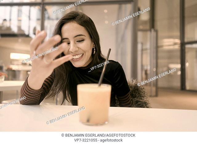 portrait of happy woman with healthy juice glass enjoying break at table in café, candid emotional expression, in Munich, Germany