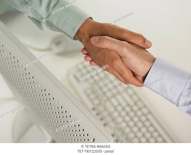 Two men shaking hands over computer