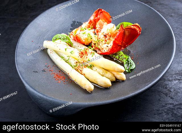 Traditional barbecue spiny lobster tail sliced and offered with white asparagus and lettuce as closeup on a modern design plate