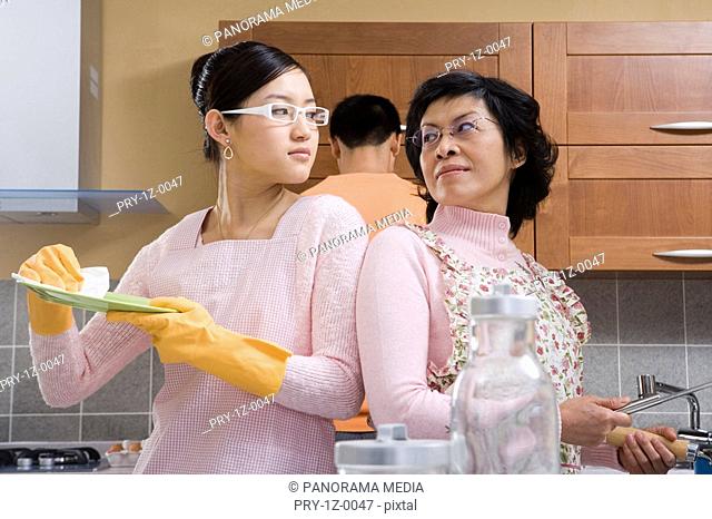 Women wearing apron looking at each other while man standing in background