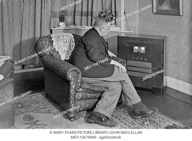 Man sitting in an armchair, listening to a large radio