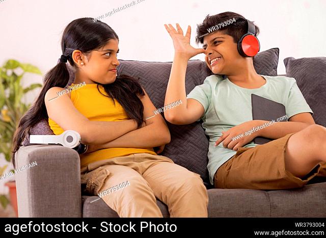 Young brother teasing his sister while sitting on sofa with digital tabletin living room