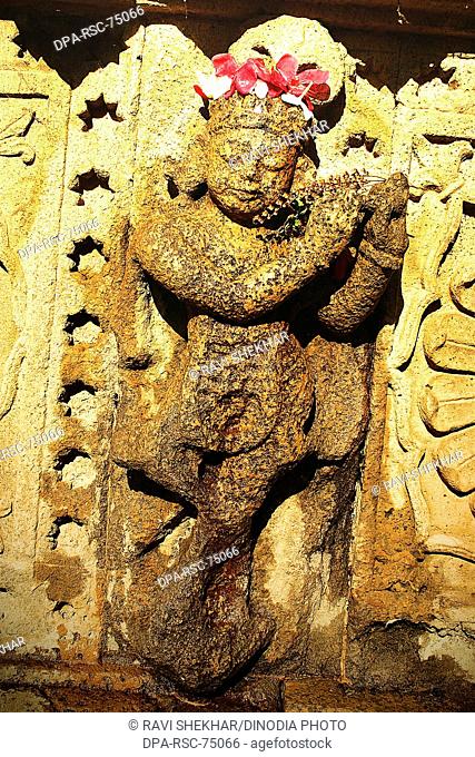Indian God Krishna playing flute , carved on the wall of Ahilayabai temple , with red flowers for worshiping in Hindu religious tradition