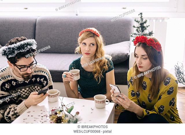 Annoyed young woman sitting between her friends looking at her smartphones