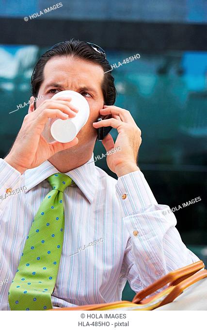 Businessman talking on a mobile phone and drinking cold drink