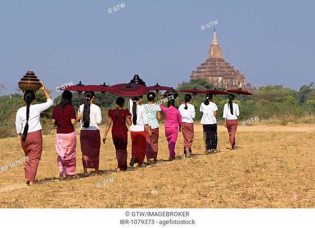 Young Burmese women with a parasol crossing a field near the Sulamani Pagoda, Bagan, Myanmar