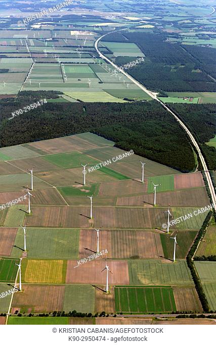Aerial view of a windfarm and wind turbines in the middle of agricultural farmland with green fields, forest and a highway passing, Lower Saxonia, Germany