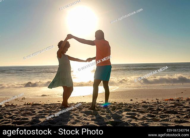 Full length of happy african american couple holding hands while dancing at beach against sky